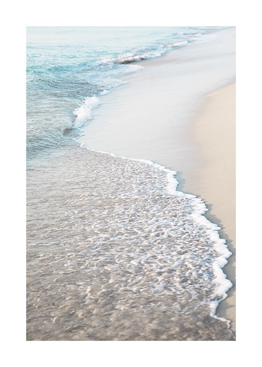  – Fotografi av en strand med ljus sand och vågor som rullar in