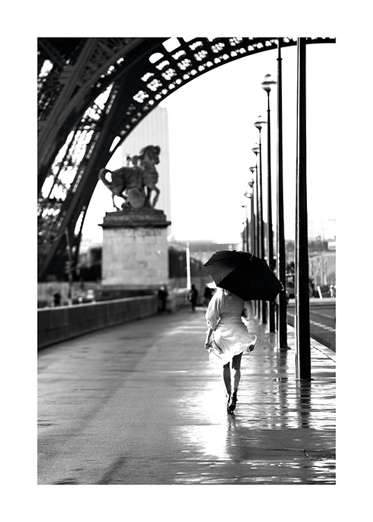  – Svartvitt fotografi av en kvinna som går med ett paraply under Eiffeltornet