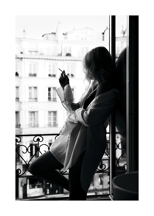  – Svartvitt fotografi av en kvinna i stor skjorta som röker en cigarett i ett fönster