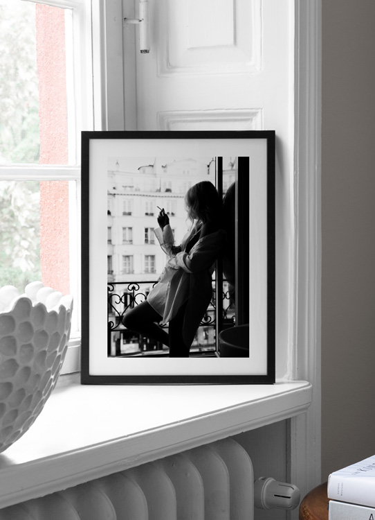  – Svartvitt fotografi av en kvinna i stor skjorta som röker en cigarett i ett fönster