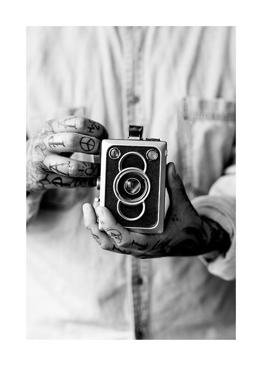  – Svartvitt fotografi av en vintagekamera som hålls av en man med tatuerade händer