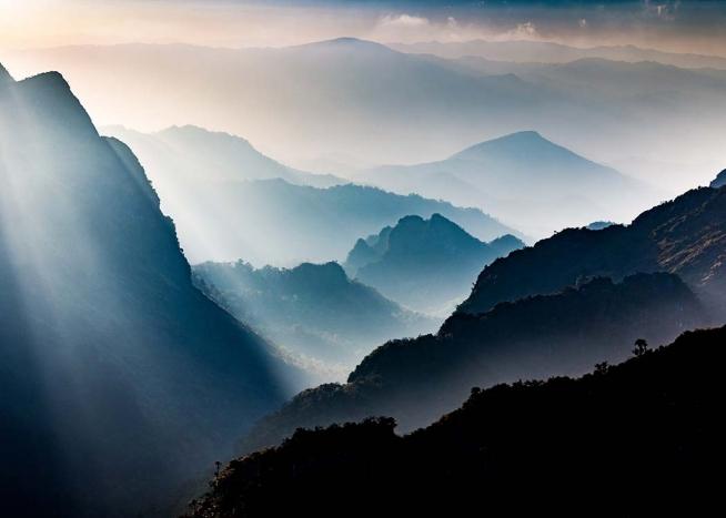 – Fotografi av dimmiga berg med solen skinande igenom.