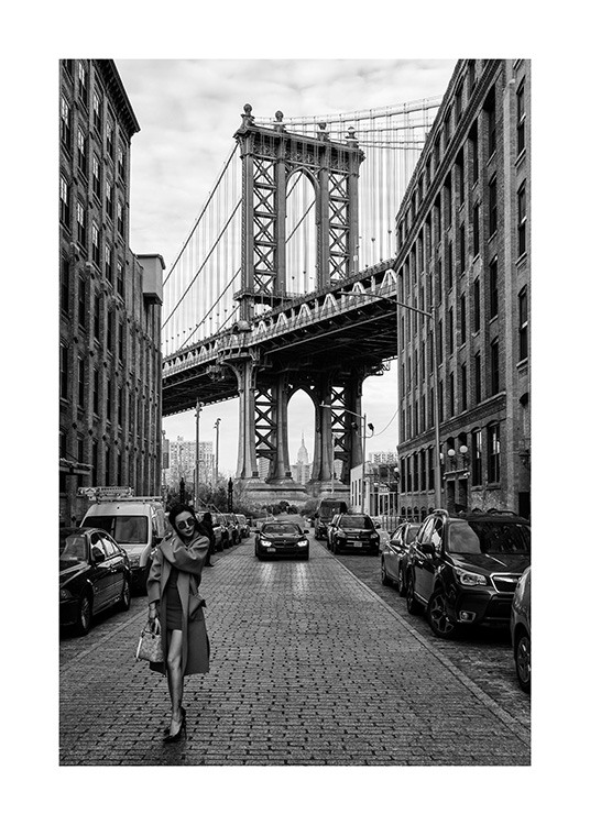 – Svartvitt fotografi av en kvinna som står på en gata i New York framför Manhattan Bridge