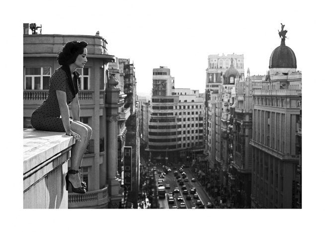 Svartvitt fotografi av kvinna tittar ner på staden från ett tak