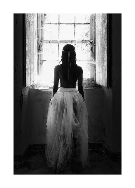 Svartvitt fotografi av kvinna i tyllkjol som står framför ett fönster