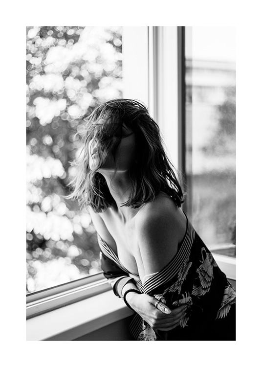 Svartvitt fotografi av kvinna som lutar sig mot en fönsterbräda iklädd en off shoulder-topp