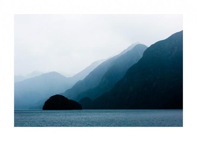  - Fotografi av havet framför blå berg med dimma bakom