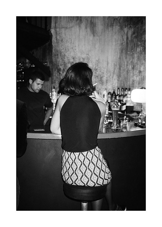  – Svartvitt fotografi av en kvinna som sitter på en barstol i en bar och röker en cigarett