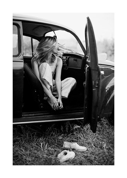  – Svartvitt fotografi av en kvinna i en veteranbil med öppen dörr och hennes skor framför bilen
