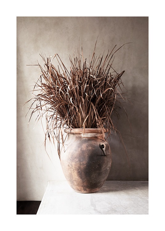  – Fotografi av torkat, beige gräs i en vas mot en betongvägg i beige