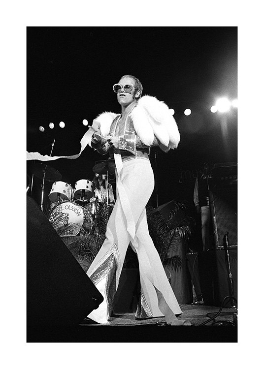  – Svartvitt fotografi av sångaren Elton John, klädd i en vit overall och solglasögon på scenen