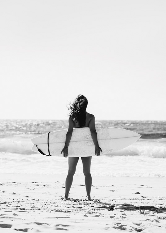  – Svartvitt fotografi av en tjej som håller en surfbräda bakom sig med havet i bakgrunden