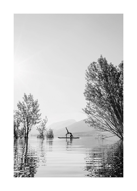  – Svartvitt fotografi av en kvinna i en yogaposition på en surfbräda mitt i en sjö