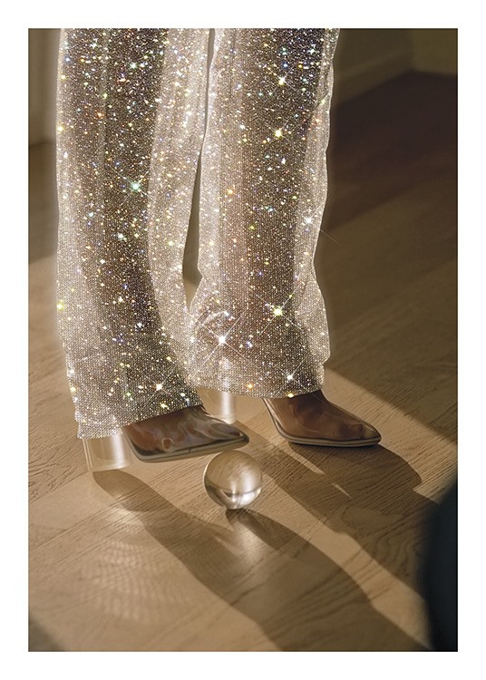  – Fotografi av en kvinna med en glasboll under skon, som bär glittrande byxor