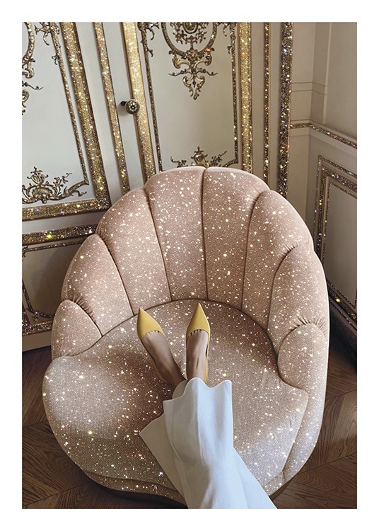  – Fotografi av en rosa, gnistrande stol framför en vägg i guld och vitt, med en kvinna som vilar fötterna på stolen