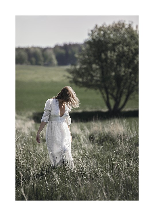  – Fotografi av en kvinna i en vit klänning som står på en gräsäng med träd i bakgrunden