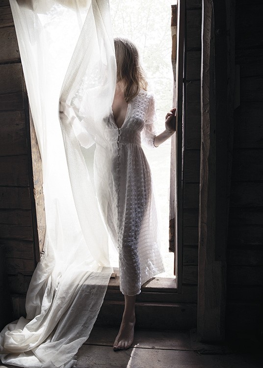  – Fotografi av en kvinna som står i en dörröppning i en vit klänning, täckt av en vit gardin