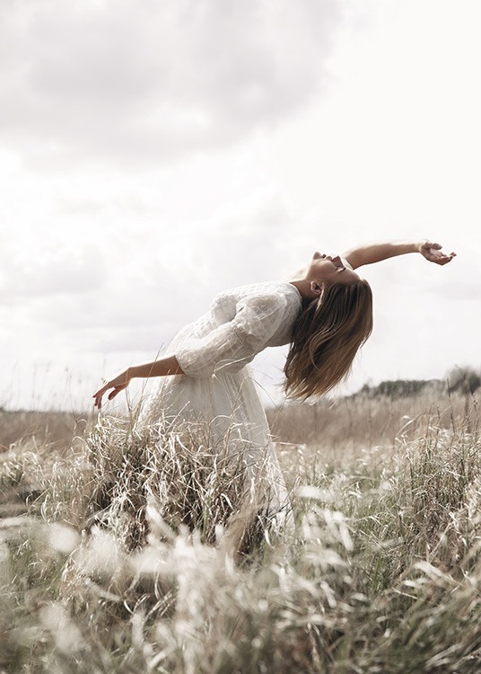  – Fotografi av en kvinna som poserar på ett fält med gräs, klädd i en vit klänning