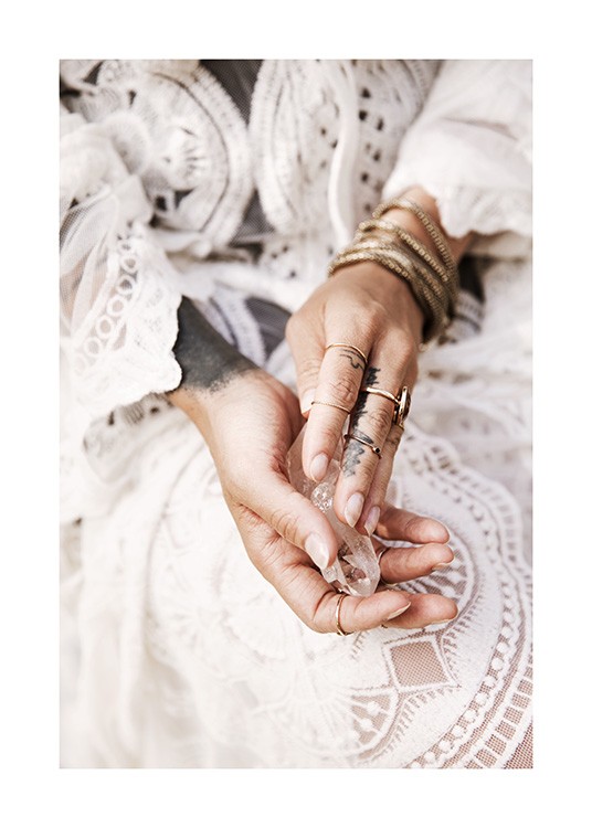  – Fotografi av händer som håller en kristall, med guldsmycken och en vit spetsklänning i bakgrunden