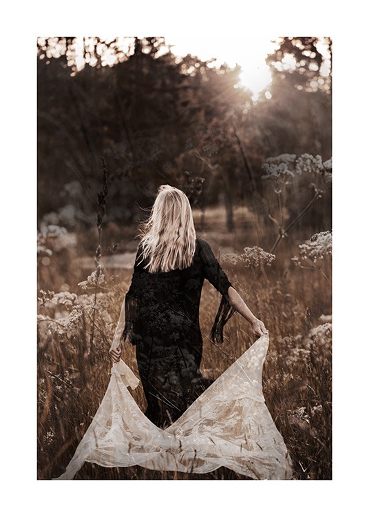  – Fotografi av en kvinna som går på en äng i en svart klänning och håller vit spets bakom sig