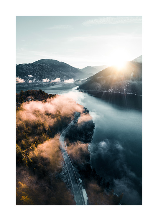  – Fotografi av ett landskap med en väg mellan en skog och en sjö med berg och solen i bakgrunden