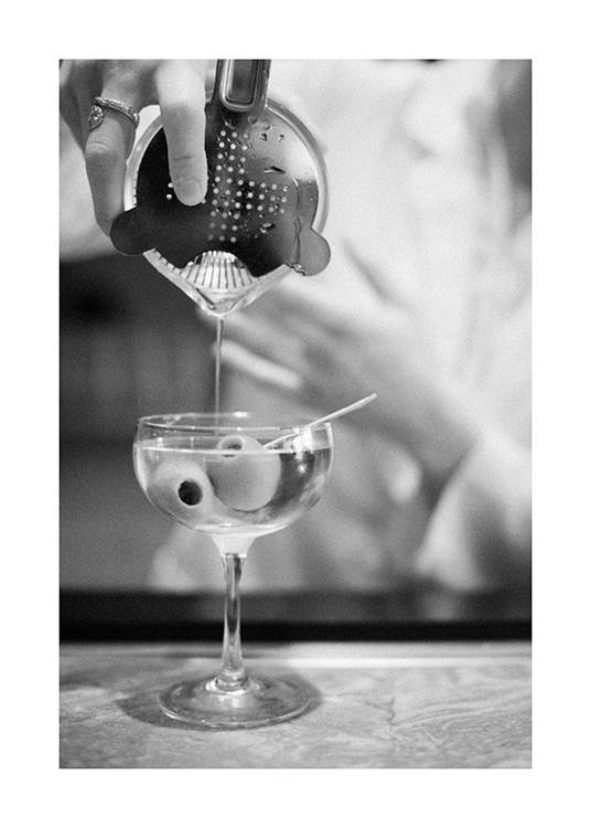  – Svartvitt fotografi av en martini som hälls från en drinkshaker, med oliver i glaset