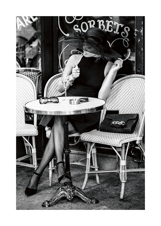  – Svartvitt fotografi av en kvinna som sitter utanför ett kafé klädd i en hatt och tänder en cigarett