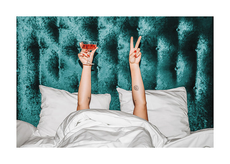  – En kvinna som håller en orange drink i en säng med en turkos sänggavel i sammet