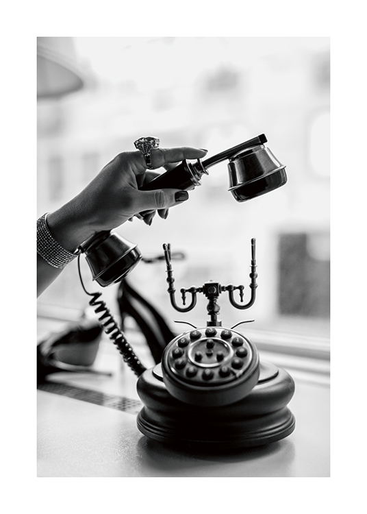  – Ett svartvitt foto av en kvinna som lyfter luren på en gammaldags telefon, med en massiv ring på fingret