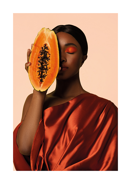  – En kvinna i satinklänning som håller en delad papaya mot ansiktet
