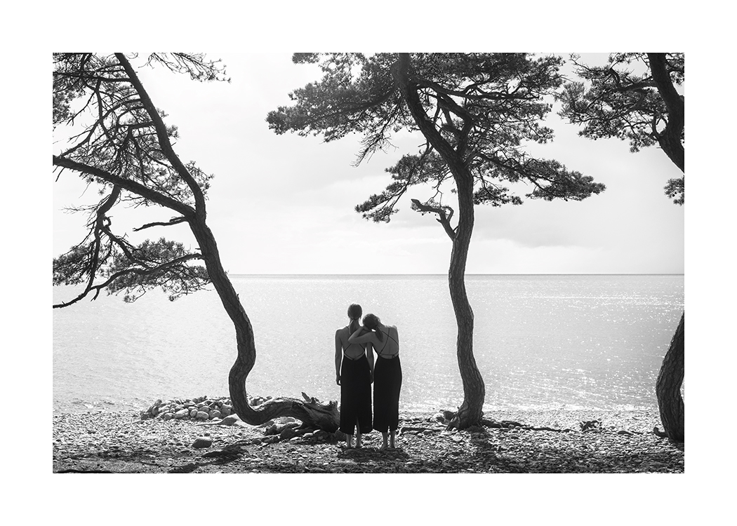  – Svartvitt fotografi av två kvinnor som tittar ut över vattnet från en strand med träd