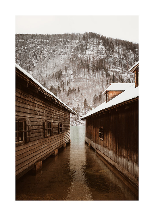  – Fotografi av två båthus framför ett berg med en snöig skog