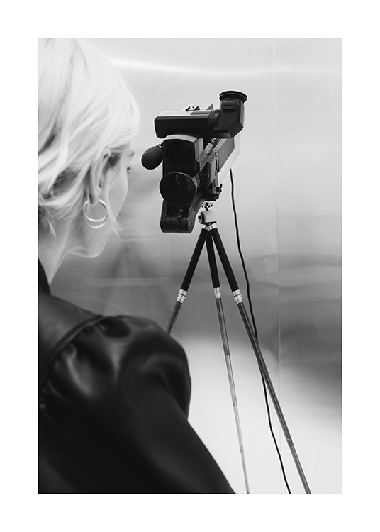  – Svartvitt fotografi av en kvinna med blont hår som står bakom en videokamera